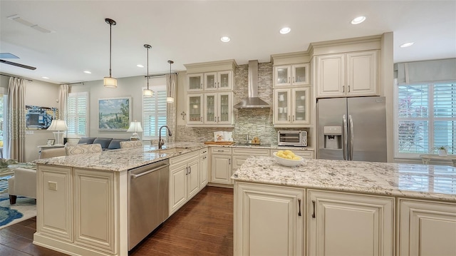 kitchen featuring dark hardwood / wood-style floors, wall chimney range hood, pendant lighting, sink, and appliances with stainless steel finishes