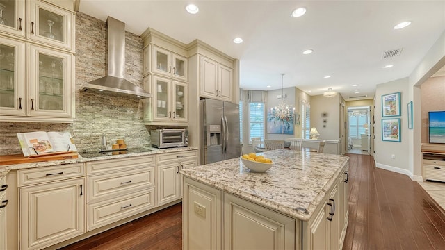 kitchen with decorative light fixtures, wall chimney range hood, decorative backsplash, stainless steel fridge with ice dispenser, and cream cabinetry