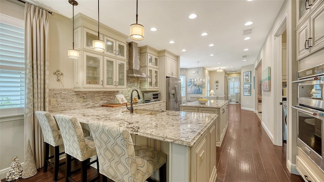 kitchen with appliances with stainless steel finishes, wall chimney range hood, pendant lighting, a breakfast bar, and sink