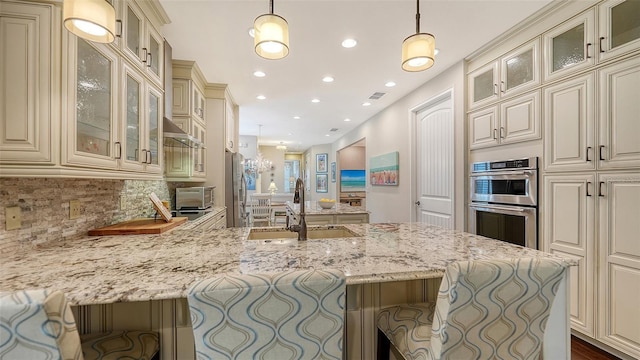 kitchen with decorative light fixtures, tasteful backsplash, appliances with stainless steel finishes, a kitchen breakfast bar, and cream cabinets