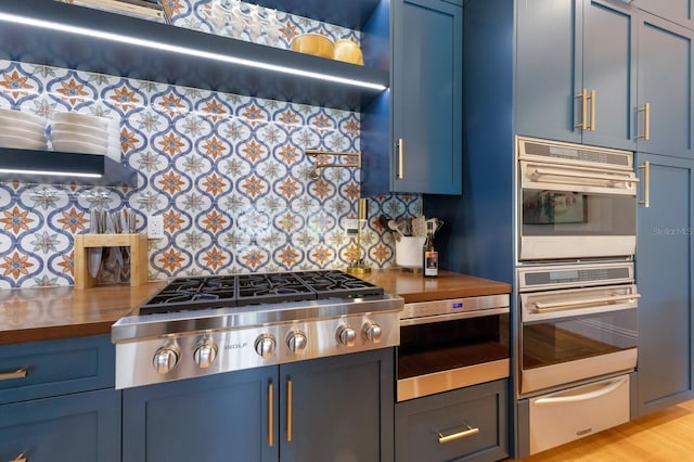 kitchen with wood counters, appliances with stainless steel finishes, blue cabinets, and tasteful backsplash