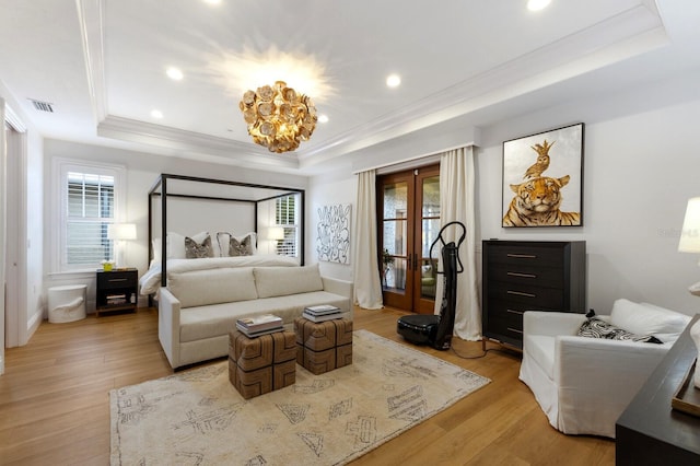 bedroom featuring light hardwood / wood-style floors, a raised ceiling, ornamental molding, french doors, and a chandelier