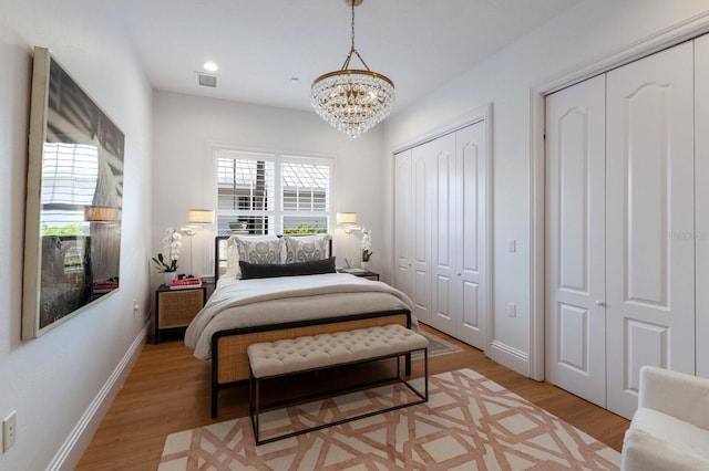 bedroom with light wood-type flooring, an inviting chandelier, and two closets