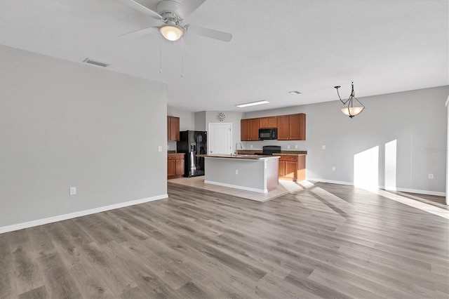 kitchen featuring ceiling fan, light hardwood / wood-style floors, decorative light fixtures, a center island with sink, and black appliances