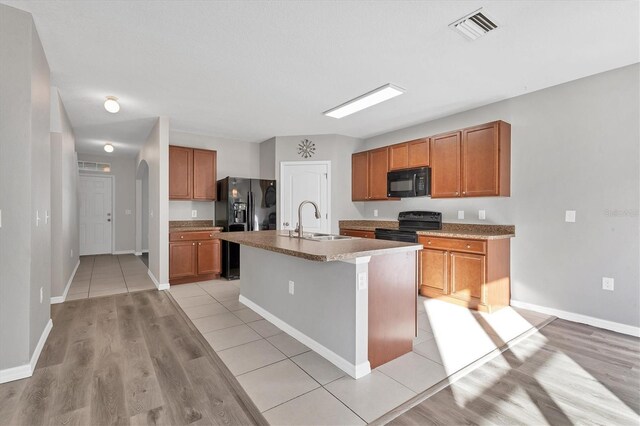 kitchen with black appliances, sink, a kitchen island with sink, and light hardwood / wood-style flooring