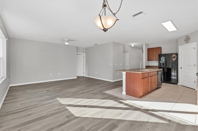 kitchen featuring light wood-type flooring, ceiling fan, black appliances, decorative light fixtures, and an island with sink