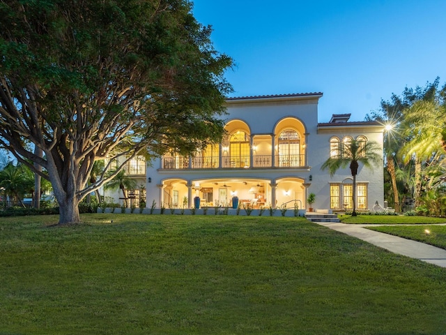 back house at dusk featuring a lawn, a balcony, and french doors