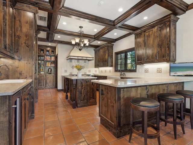 kitchen with coffered ceiling, sink, beamed ceiling, a kitchen island, and dark brown cabinetry