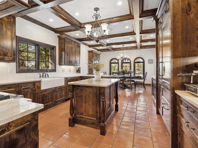 kitchen with coffered ceiling, dark brown cabinetry, an inviting chandelier, a kitchen island, and hanging light fixtures