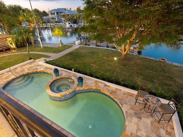 pool at dusk featuring an in ground hot tub, a yard, a water view, and a patio