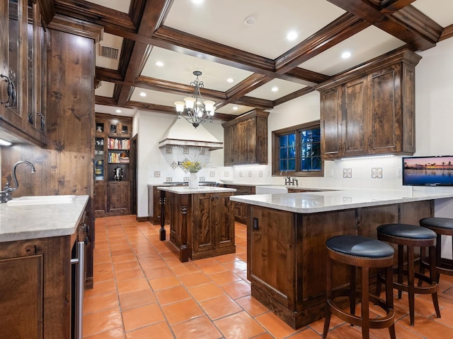 kitchen featuring beamed ceiling, dark brown cabinets, a kitchen island, and sink