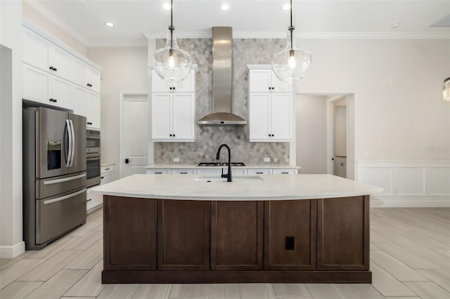 kitchen with a center island with sink, wall chimney exhaust hood, stainless steel appliances, and hanging light fixtures