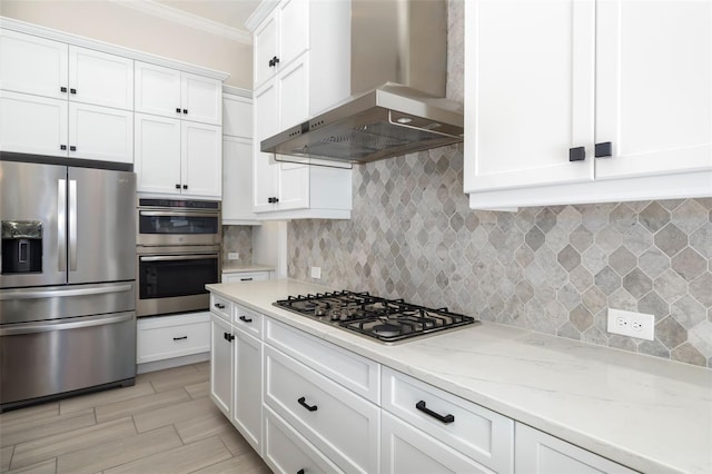 kitchen featuring wall chimney exhaust hood, stainless steel appliances, tasteful backsplash, crown molding, and white cabinets