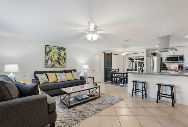 living room featuring ceiling fan, light tile patterned floors, and a barn door