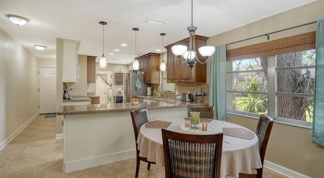 kitchen with stainless steel refrigerator, sink, light stone counters, kitchen peninsula, and decorative backsplash