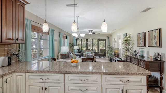 kitchen featuring tasteful backsplash, ceiling fan, light stone countertops, and decorative light fixtures