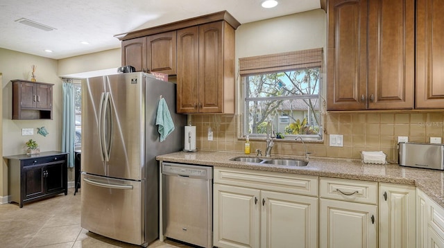 kitchen with backsplash, sink, light stone countertops, appliances with stainless steel finishes, and light tile patterned flooring