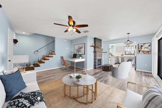 living room featuring ceiling fan with notable chandelier, light hardwood / wood-style floors, and a stone fireplace