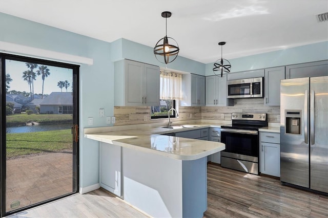 kitchen with sink, backsplash, stainless steel appliances, kitchen peninsula, and hanging light fixtures