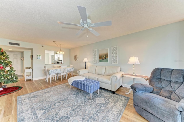 living room featuring ceiling fan with notable chandelier, a textured ceiling, and light wood-type flooring