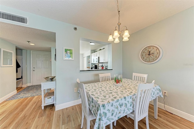 dining space with a notable chandelier, light hardwood / wood-style floors, and a textured ceiling