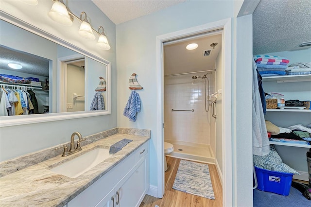 bathroom featuring vanity, toilet, tiled shower, a textured ceiling, and wood-type flooring