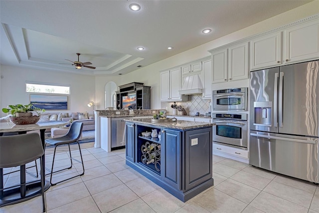 kitchen with a center island, white cabinetry, light stone counters, a raised ceiling, and appliances with stainless steel finishes