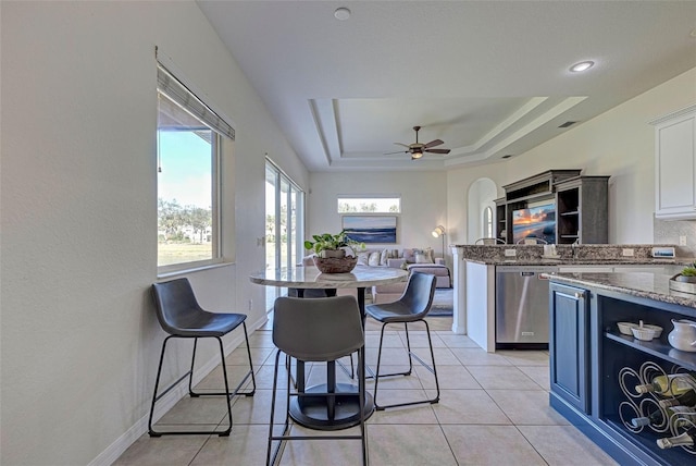 kitchen featuring white cabinets, dishwasher, light tile patterned floors, a tray ceiling, and a breakfast bar