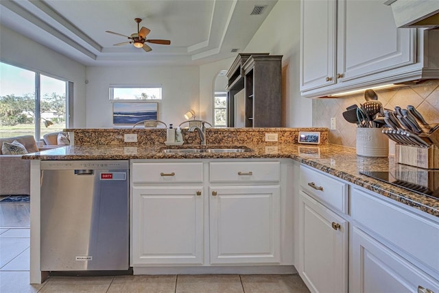 kitchen with stainless steel dishwasher, a tray ceiling, white cabinets, dark stone counters, and sink