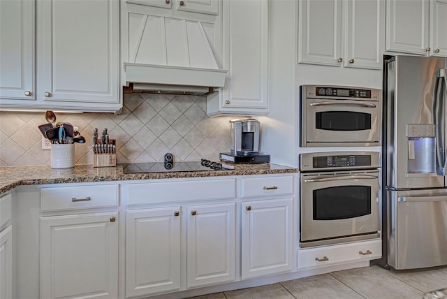 kitchen featuring stainless steel appliances, premium range hood, dark stone countertops, and white cabinetry