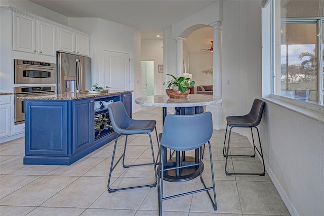 kitchen with ornate columns, stainless steel fridge with ice dispenser, a center island, white cabinets, and blue cabinets