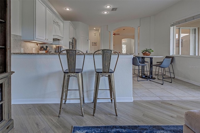 kitchen featuring kitchen peninsula, light stone countertops, white cabinetry, ceiling fan, and a kitchen breakfast bar