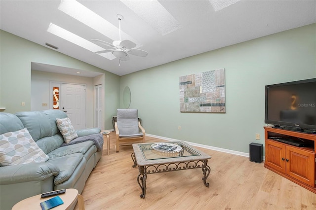 living room with ceiling fan, light hardwood / wood-style flooring, and vaulted ceiling with skylight