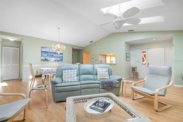 living room with a textured ceiling, lofted ceiling, light wood-type flooring, and ceiling fan with notable chandelier