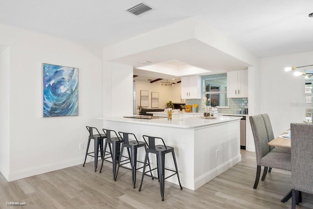 kitchen featuring white cabinets, light hardwood / wood-style flooring, tasteful backsplash, kitchen peninsula, and a breakfast bar area