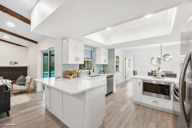 kitchen featuring appliances with stainless steel finishes, sink, light hardwood / wood-style flooring, white cabinetry, and hanging light fixtures