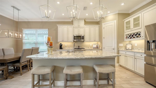 kitchen featuring appliances with stainless steel finishes, a center island with sink, light stone counters, and decorative light fixtures