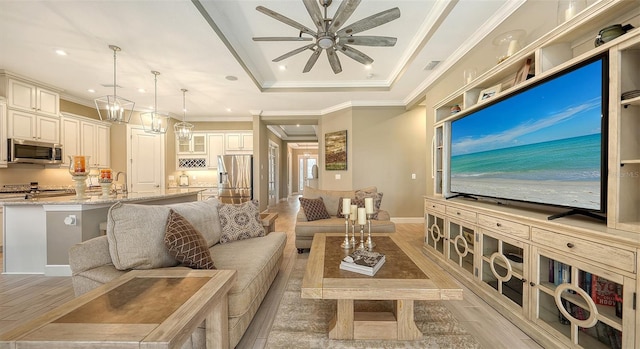 living room with ceiling fan with notable chandelier, a tray ceiling, recessed lighting, light wood-style floors, and crown molding