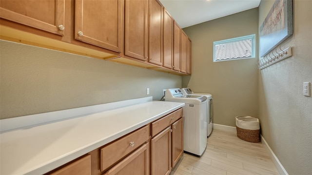 clothes washing area featuring cabinets, washer and dryer, and light hardwood / wood-style floors