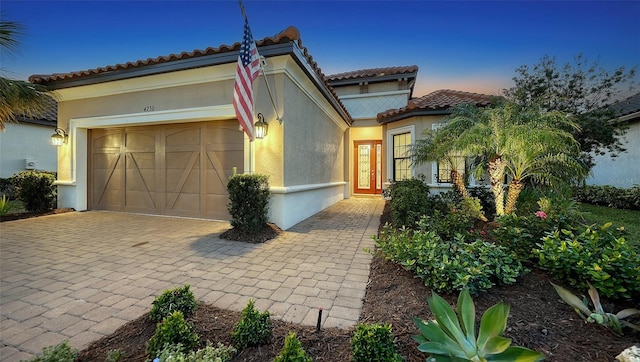 mediterranean / spanish house featuring a tiled roof, stucco siding, an attached garage, and decorative driveway