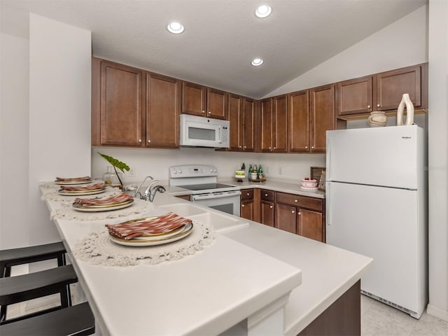 kitchen featuring kitchen peninsula, a breakfast bar, a textured ceiling, white appliances, and vaulted ceiling