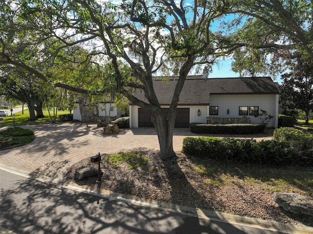 view of front facade with an attached garage, stone siding, a shingled roof, and decorative driveway