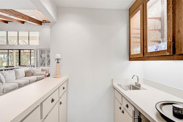 kitchen featuring white cabinets, glass insert cabinets, beamed ceiling, light countertops, and a sink