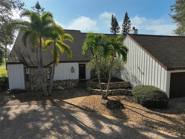 back of house featuring a shingled roof, stone siding, a chimney, and board and batten siding