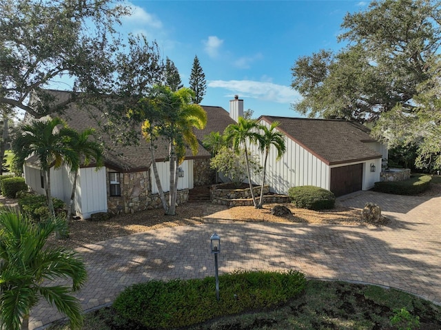 view of front of property featuring stone siding, a chimney, decorative driveway, and roof with shingles