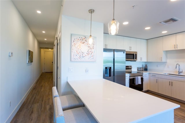 kitchen with sink, hanging light fixtures, dark hardwood / wood-style floors, a breakfast bar, and appliances with stainless steel finishes