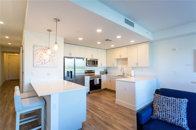 kitchen with pendant lighting, white cabinets, appliances with stainless steel finishes, light hardwood / wood-style floors, and kitchen peninsula