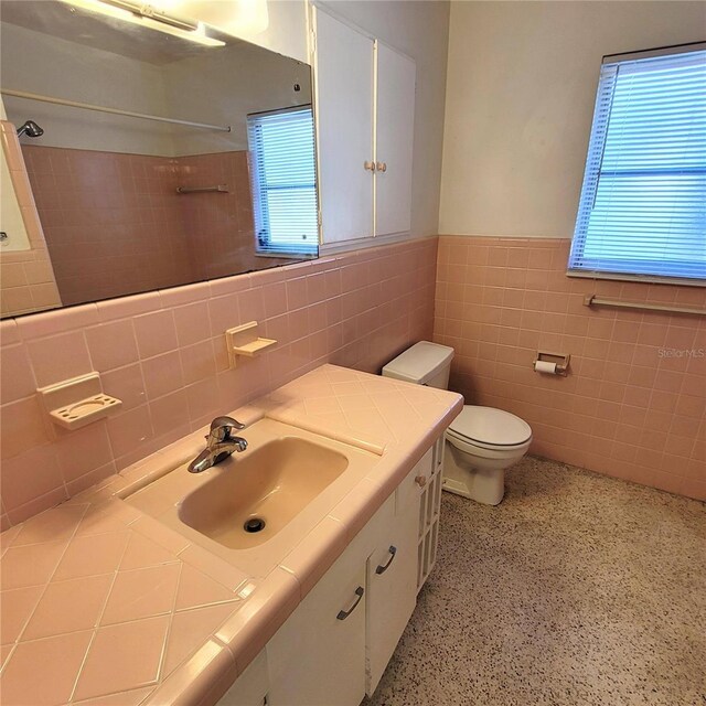 bathroom featuring vanity, toilet, a wealth of natural light, and tile walls