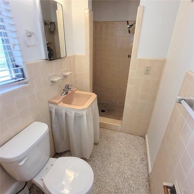 bathroom with a tile shower, tile walls, and toilet