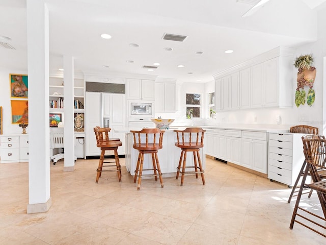 kitchen with built in appliances, a center island, white cabinets, and a kitchen bar